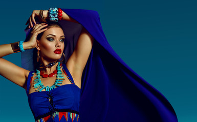 beautiful young girl in bright blue attire and a lot of jewelry on the background of a bright sky....