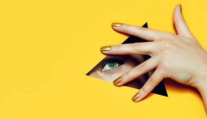 A girl with beautiful long fingers and gold nail varnish covers her eyes in a triangular hole of orange paper.