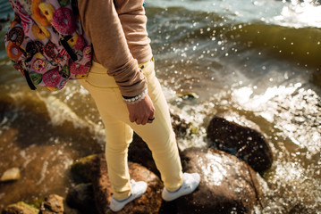 Young girl with a backpack standing on a stone on the beach