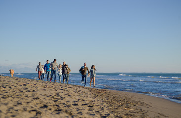 Group of friends running on beach during autumn day