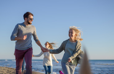 Group of friends running on beach during autumn day