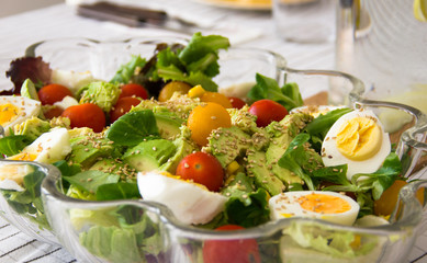 Delicious salad glass bowl with spinach, boiled eggs, cherry tomatoes, avocado pieces and sesame seeds on table. Healthy eating, vegetarian food concepts