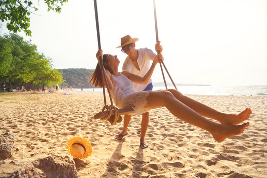 Romantic couple in love playing together on rope swing at summer beach for fun and happy smile. young man and woman on holidays or honeymoon