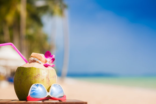 Fresh coconut cocktail decorated with orchid flower and sunglasses on a tropical beach