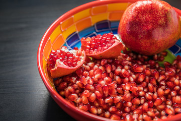 Delicious pomegranate seeds placed in glass jar with fresh organic pomegranates on rustic wooden background.Close up,Copy space