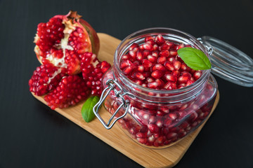 Delicious pomegranate seeds placed in glass jar with fresh organic pomegranates on rustic wooden background.Close up,Copy space