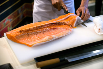 Chef cutting fresh salmon fillet in kitchen for cooking