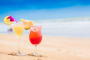 two perfect cocktails strawberry daiquiri and Margarita with lime and pineapple on top, beach background