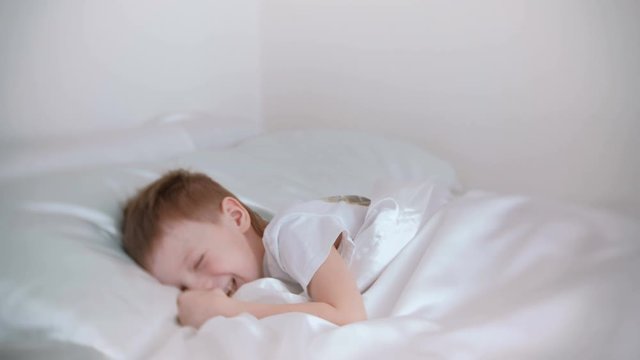 Seven-year-old boy just woke up and laughs while lying in bed.
