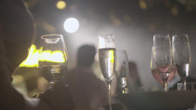 Waiter served champagne glasses on a tray in a fine dining restaurant during concert with bright spotlights in the background.