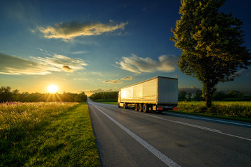Truck driving towards the setting sun on an asphalt road in rural countryside