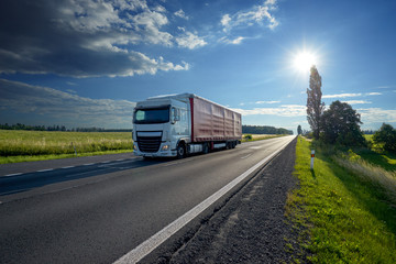 Truck driving on asphalt road under the glowing sun in the rural landscape