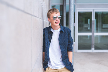 Happy teen wearing sunglasses and leaning against a brick wall.