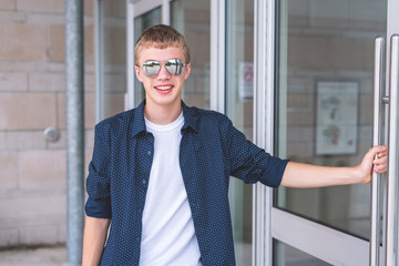 Happy teen wearing sunglasses and opening a glass door to a building.