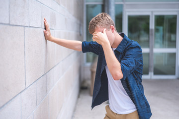 Upset teen leaning against a brick wall outside of a public building.