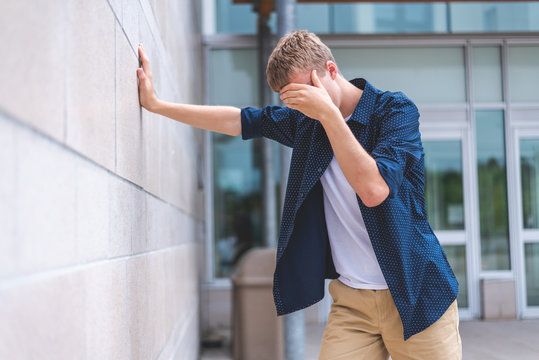 Upset Teen Leaning Against A Brick Wall Outside Of A Public Building.