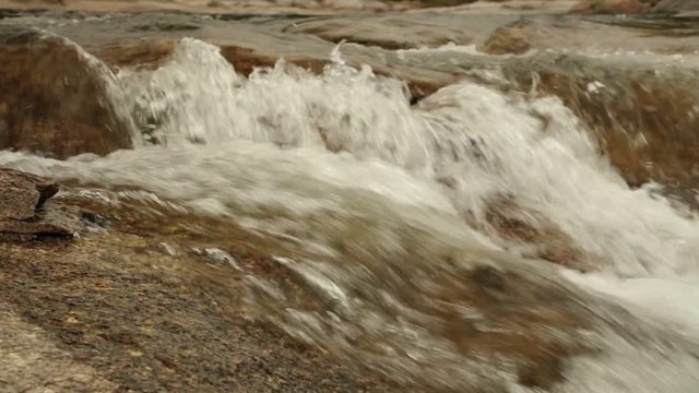 Rugged mountain river scenery panning panoramic with clear rushing mountain water running around large boulders, high definition stock footage movie clip.