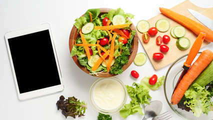 Tablet with blank screen and mixed vegetables salad on white background.
