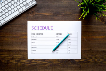 College or school schedule with lessons and bell time. Student planner on dark wooden work desk with computer and pen top view space for text