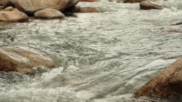 Rugged mountain river scenery panning panoramic with cascading mountain water running around large pebbles, boulders, high definition stock footage movie clip.