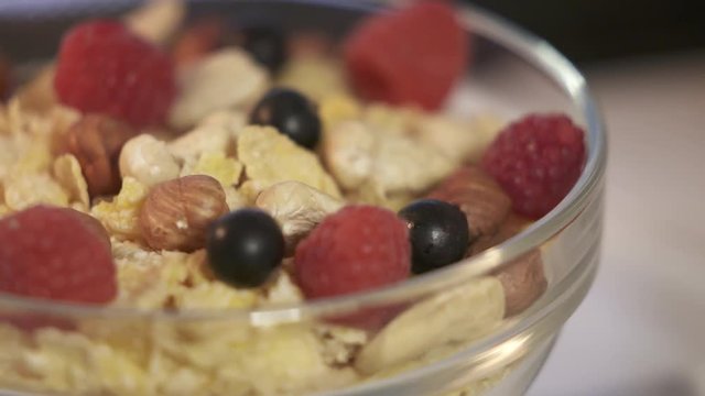 Rotating corn flakes with nuts and fresh berries in a glass bowl