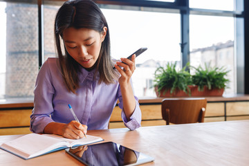 Young businesswoman using loudspeaker on mobile phone, working in cafe