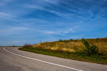 Empty asphalt road over field of grass during summer
