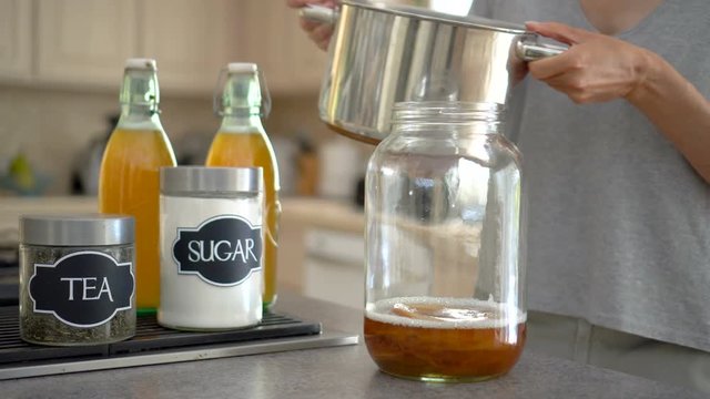 Female pours black tea into the big jar containing kombucha scoby.