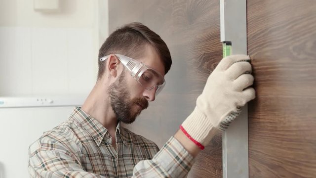 An adult engineer in uniform measures a brick wall with a level, an architect in a protective helmet checks the data of a building instrument