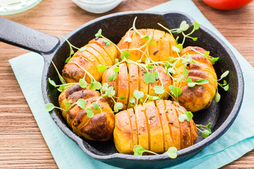 Baked young potatoes in spices and oil with arugula in a iron pan on a wooden table