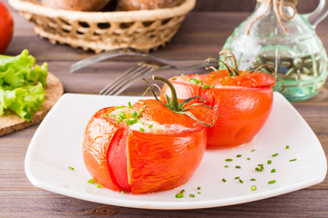 Fresh tomatoes baked with cheese and egg sprinkled with green onions on a plate on a wooden table