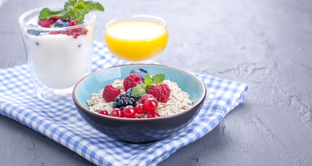 Delicious and healthy breakfast, gray background and napkin. Yogurt, muesli, granola, raspberry and blueberry berries and fresh orange juice. Copy space,