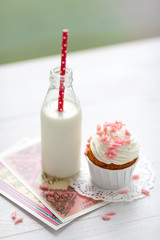 Sweet food composition with creamy cupcake with rose chocolate decoration and a bottle with fresh milk cocktail 