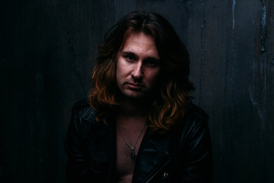 brutal man in a leather jacket on a naked body with long hair. a lonely man is sad and desperate
