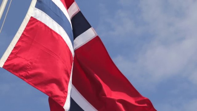 Sunlit Norwegian flag waving in the wind against a hazy blue sky