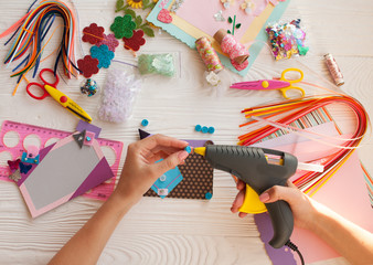 Top view of table with elements for scrapbooking, tools for decoration and handmade albums and hands of master.