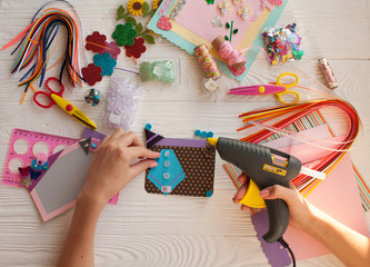 Top view of table with elements for scrapbooking, tools for decoration and handmade albums and hands of master.