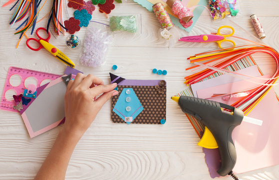 Top view of table with elements for scrapbooking, tools for decoration and handmade albums and hands of master.