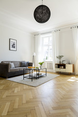 Lamp above carpet with table in spacious living room interior with grey couch and poster. Real photo