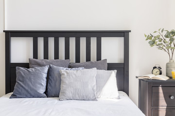 Grey and white pillows on bed with black headboard in simple bedroom interior. Real photo