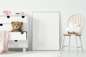 Mockup of empty poster and cabinet with plush toy and pink blanket in white child's room interior....