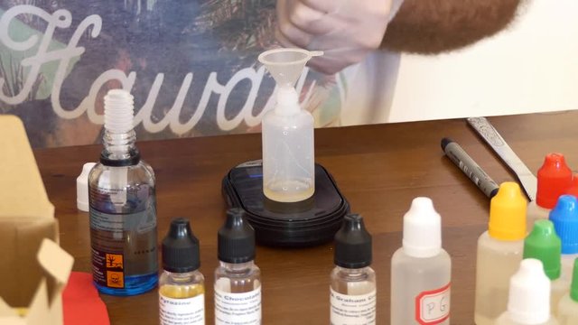 Close up of a man in latex gloves mixing different flavors to create an eliquid for vaping on an electric cigarette.