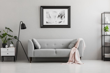 Industrial black floor lamp and a pink blanket on an elegant settee with cushions in a gray living...