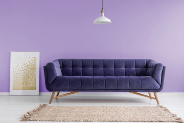Purple, velvet sofa and a beige rug in a pastel lavender living room interior with a poster...