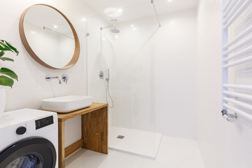 Side view of a modern bathroom interior with a shower, wash basin, round mirror, washing machine...