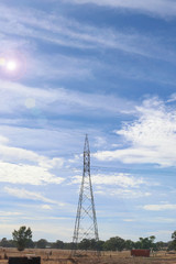 a power line support tower in a blue cloudy sky with lens flare