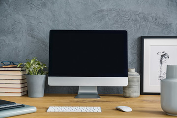 Mockup of computer desktop on wooden desk with plant in grey workspace interior. Real photo