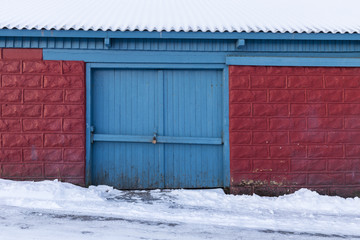 Locked gate of old wooden shed, red bricks with blue door in winter snow