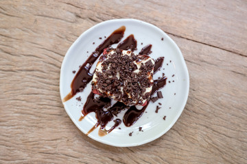 Top view image of a piece of red velvet cake with cream and chocolate in white ceramic plate on wooden table