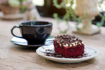A piece of red velvet cake with coffee cup on wooden table in cafe